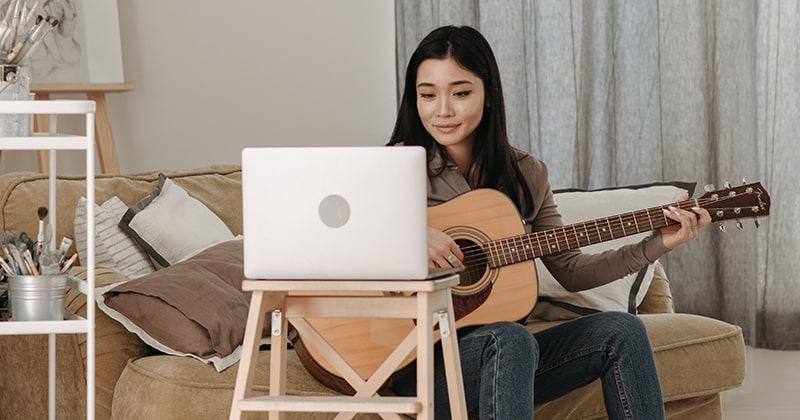 Lady learning to play the guitar from a laptop